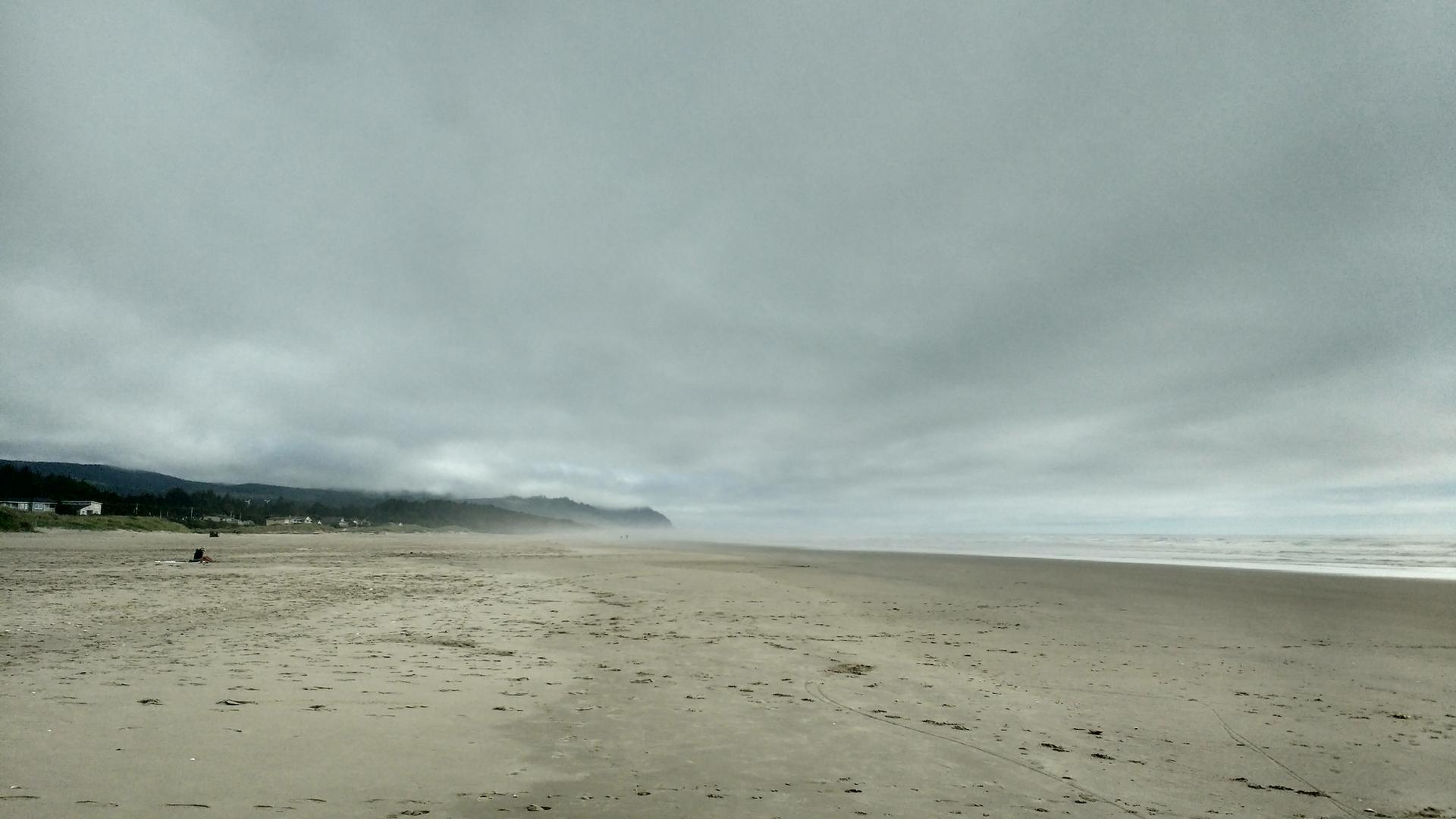 Wide, empty sandy beach under a vast, cloudy, grey sky.
