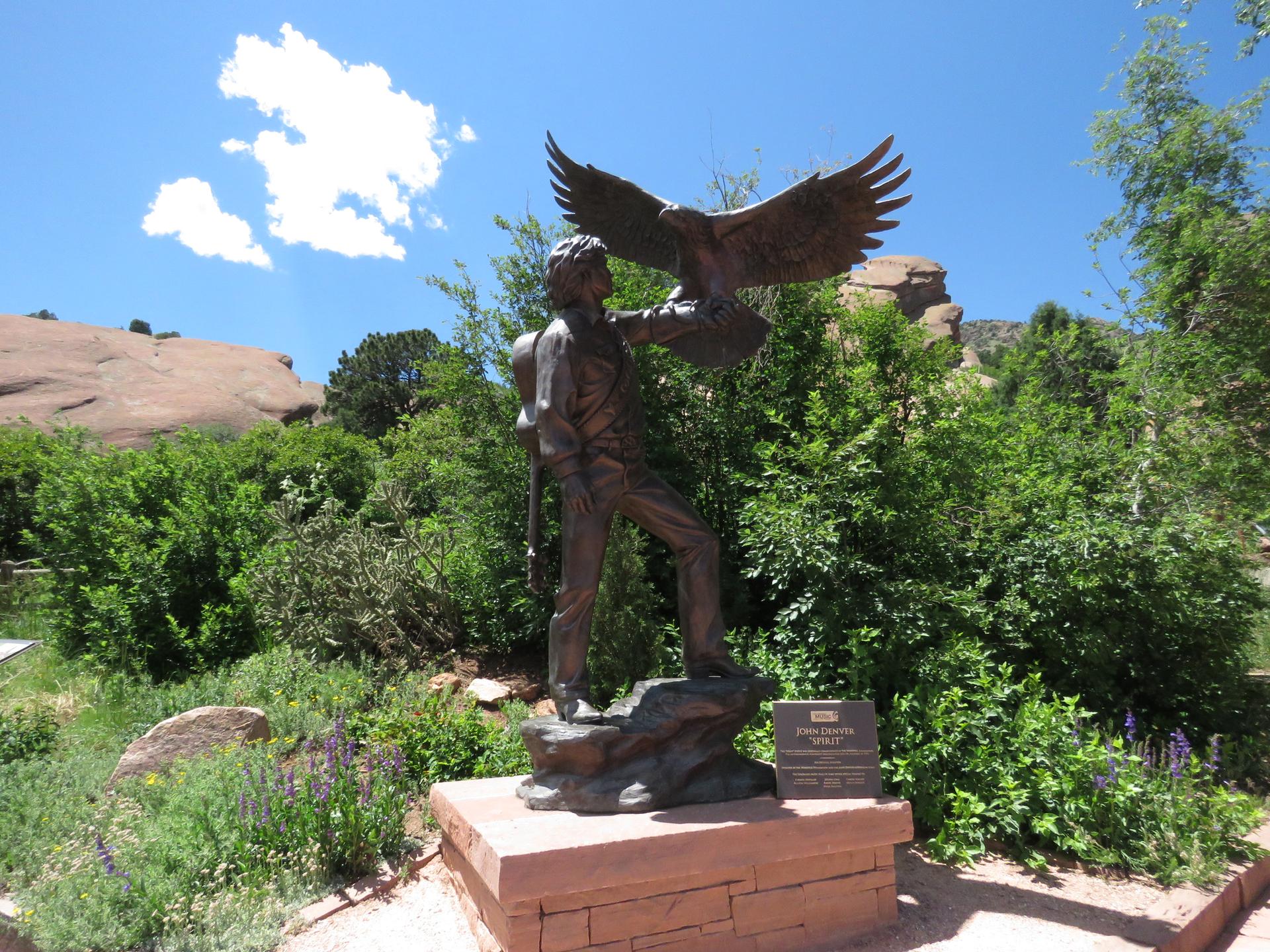 Bronze statue of a person holding an eagle, surrounded by green plants.
