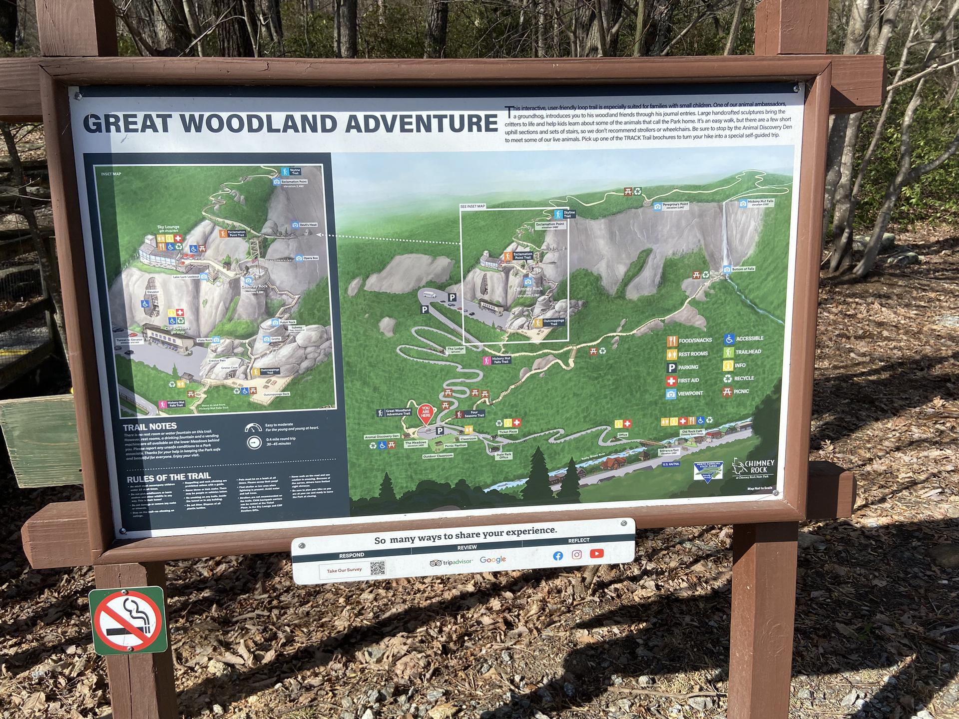Large trail map sign titled "GREAT WOODLAND ADVENTURE" in a wooded area. Bright daylight.