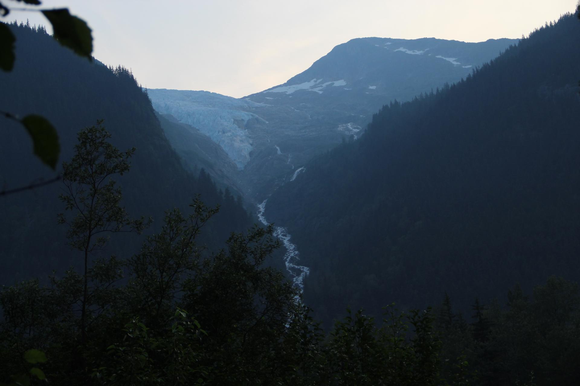 Dark mountain valley with a glacier and winding river under dim light.
