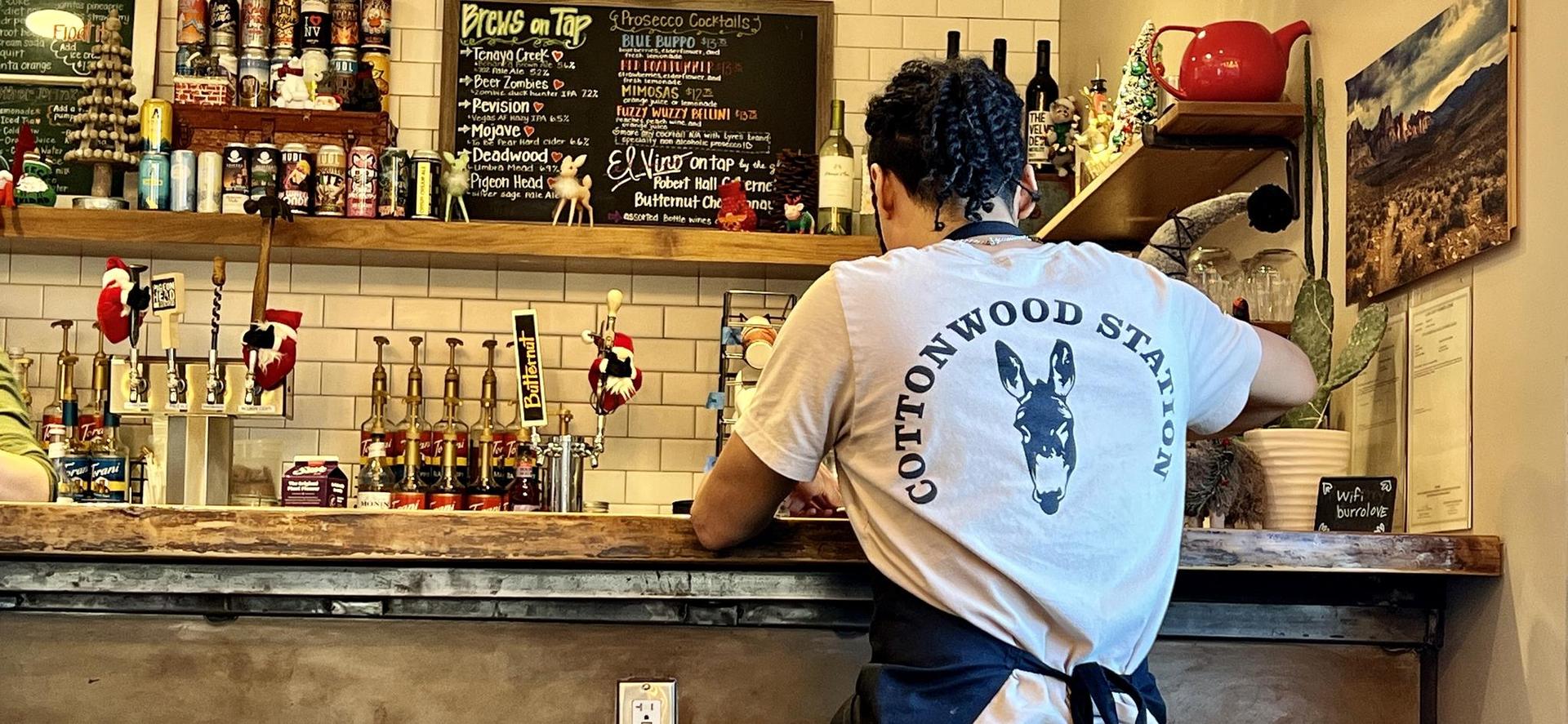 A person in a t-shirt with a donkey logo works behind a rustic bar.