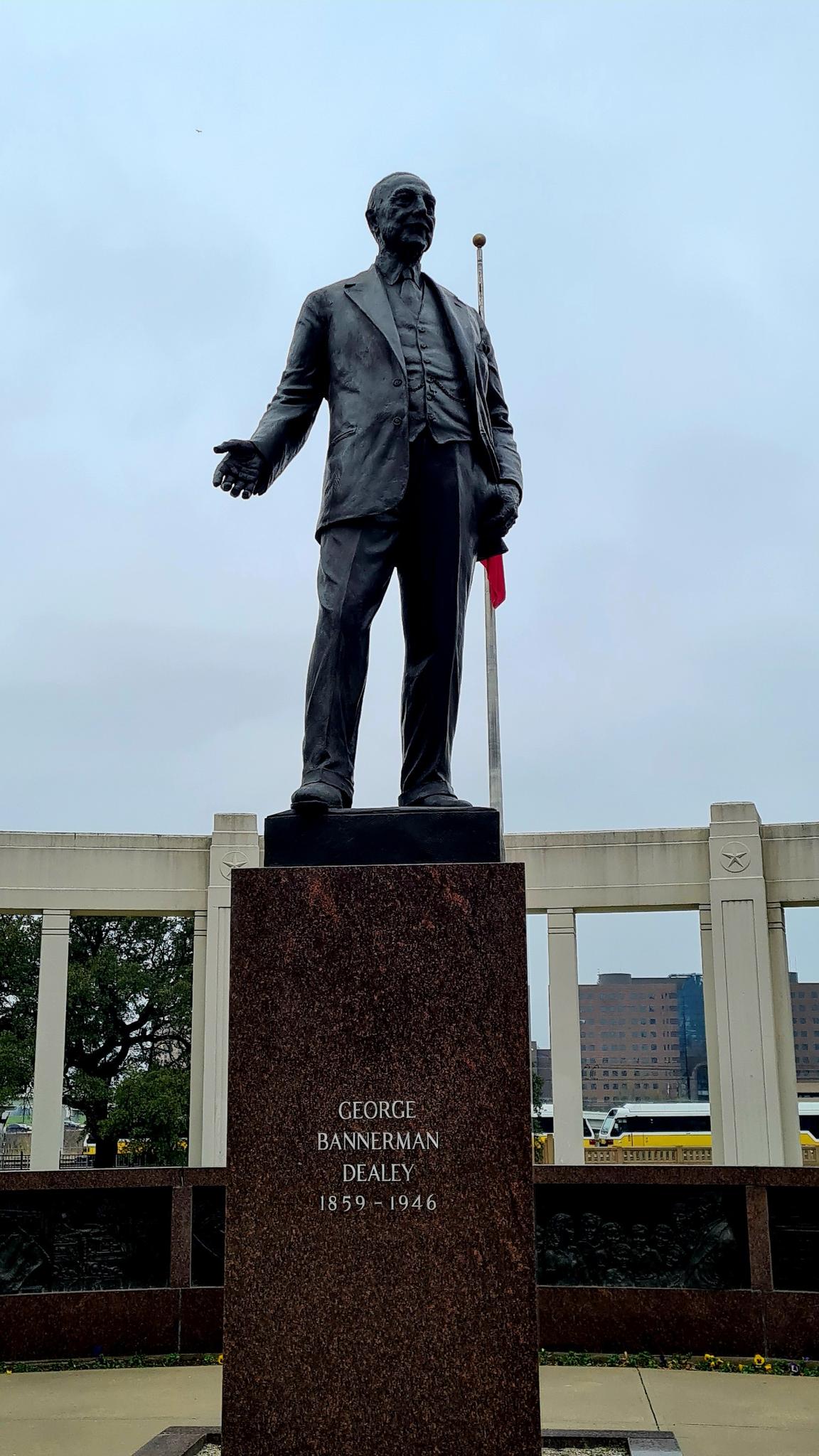 A bronze statue of a man in a suit stands on a tall stone pedestal.