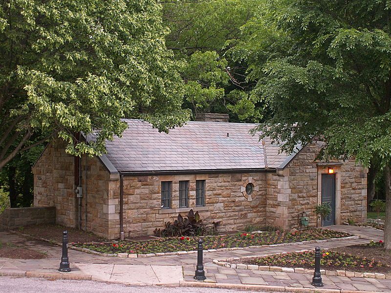 Small stone building with a gray roof surrounded by trees and flower beds. - Observatory Trail