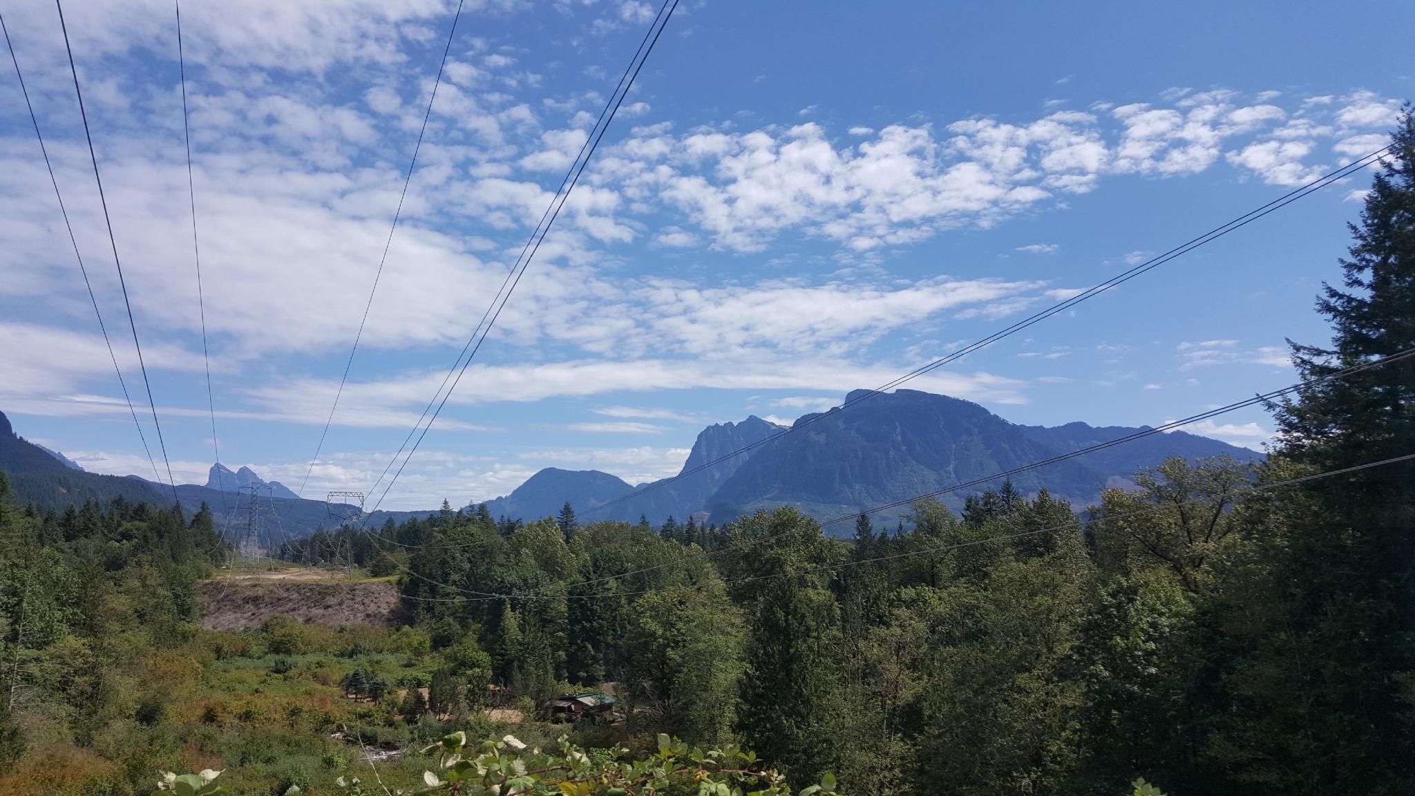 A wide view of distant mountains over a green forest under a cloudy sky. - Railroad Grade Trail