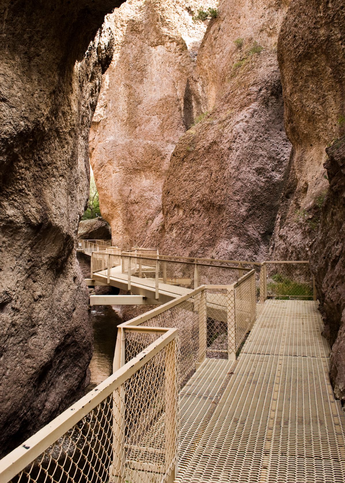Metal boardwalk winding through a narrow, rugged rock canyon with a stream below. - Catwalk National Recreation Trail
