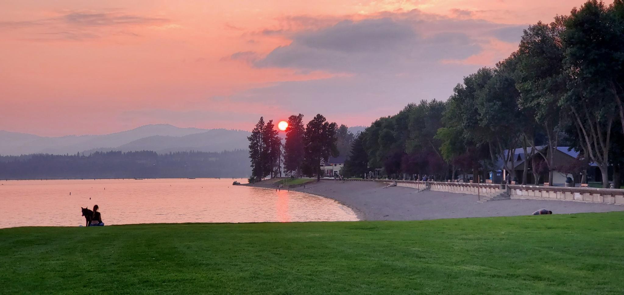 Beautiful sunset over a lake with a beach, green lawn, and two people.