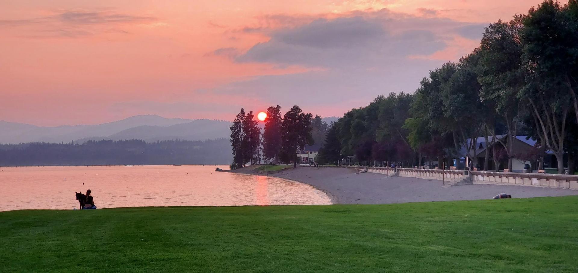 Beautiful sunset over a lake with a beach, green lawn, and two people.
