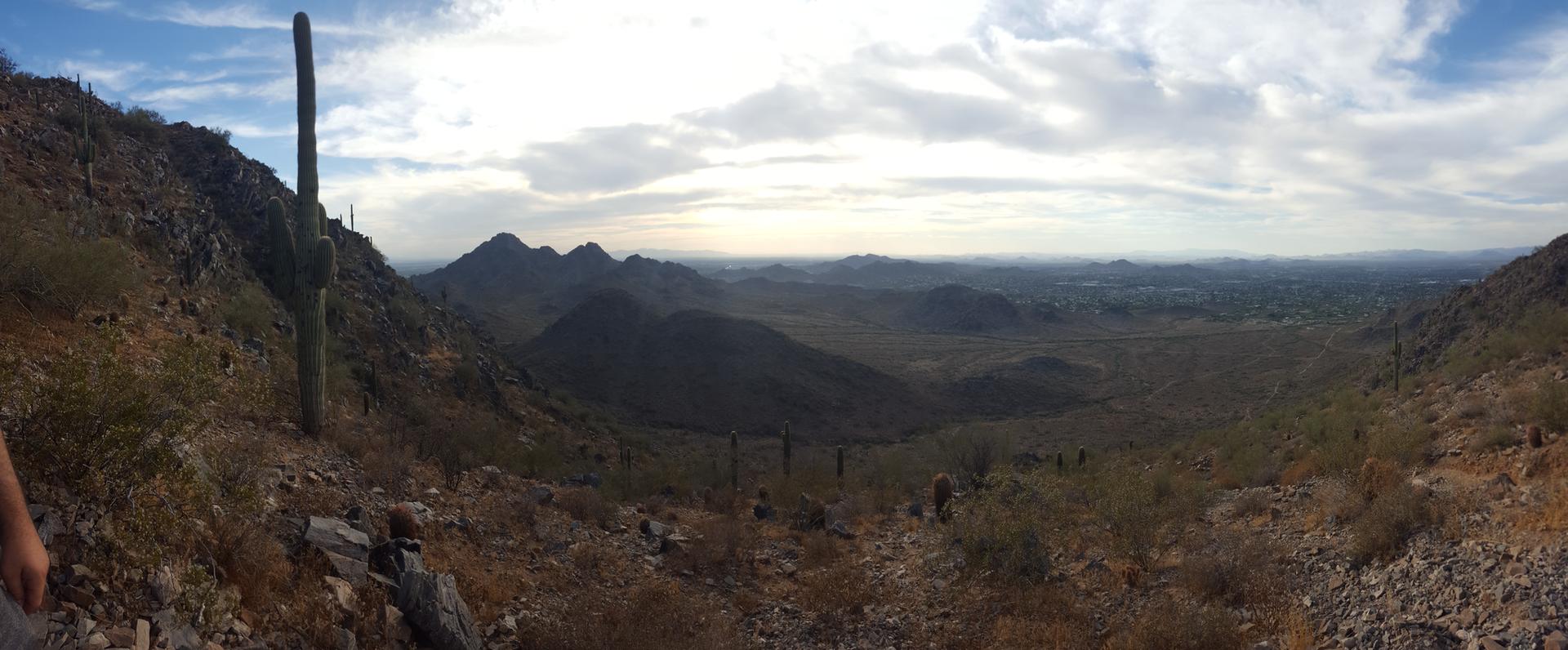 Panoramic desert landscape with saguaro cactus, rocky hills, and cloudy sky.
