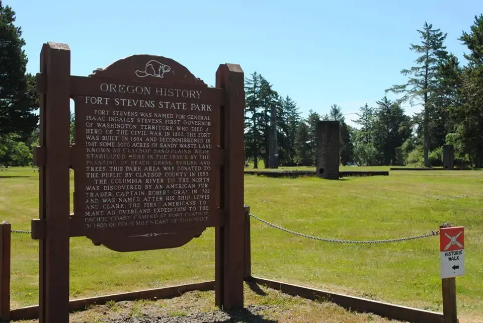 A brown historical sign stands in a sunny, grassy park.