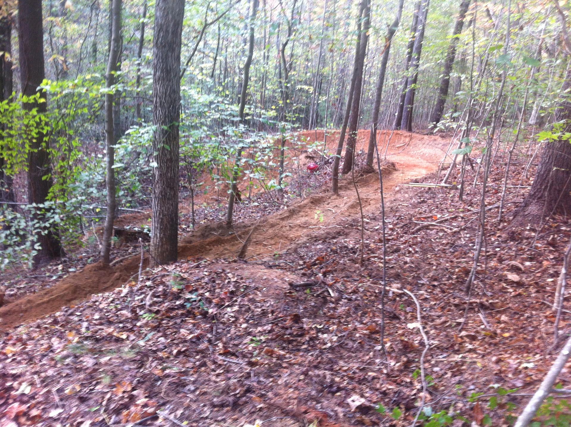 A winding dirt trail with berms through a dense forest.
