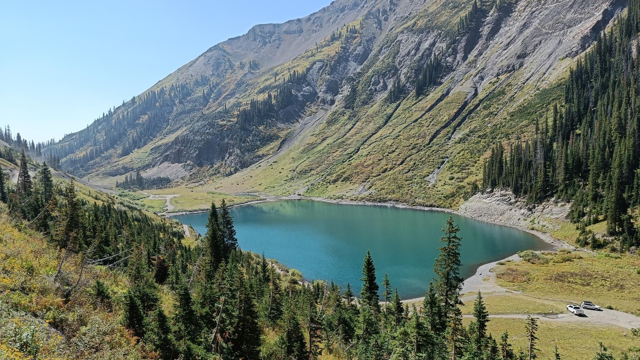 Brightly lit blue lake in a mountain valley with pine trees and vehicles. - Trail 401 Loop