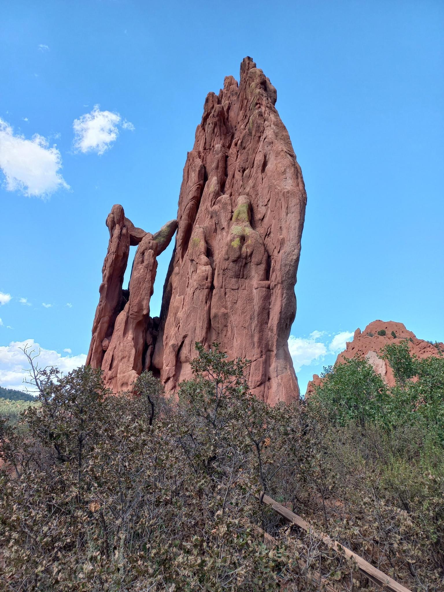 A tall, slender red rock formation with an arch under a bright blue sky.