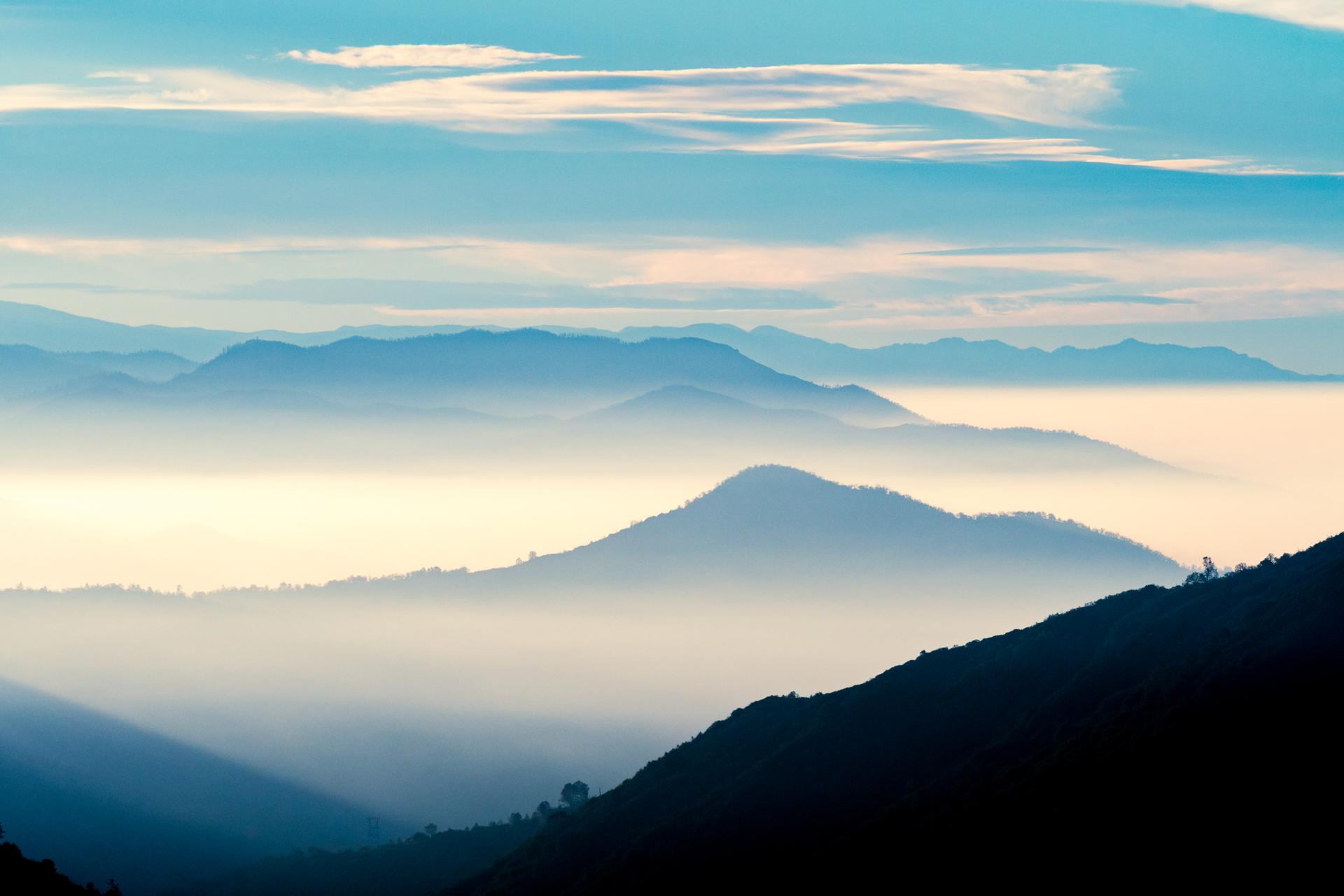 Layered mountains emerging from a sea of fog under a bright sky.