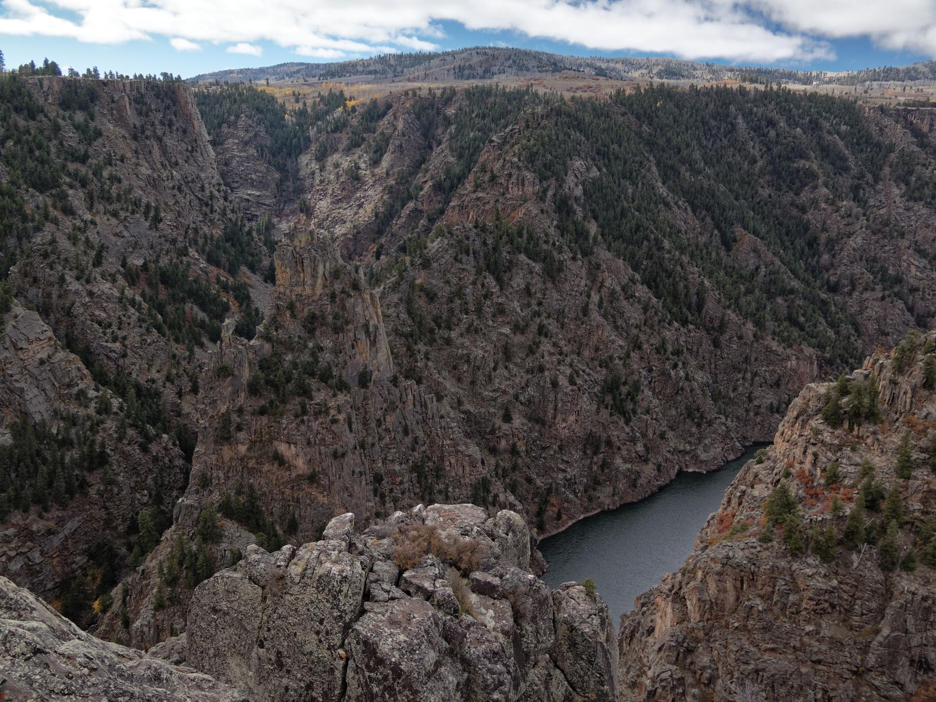 A vast, dark canyon with a river below, under a partly cloudy sky.