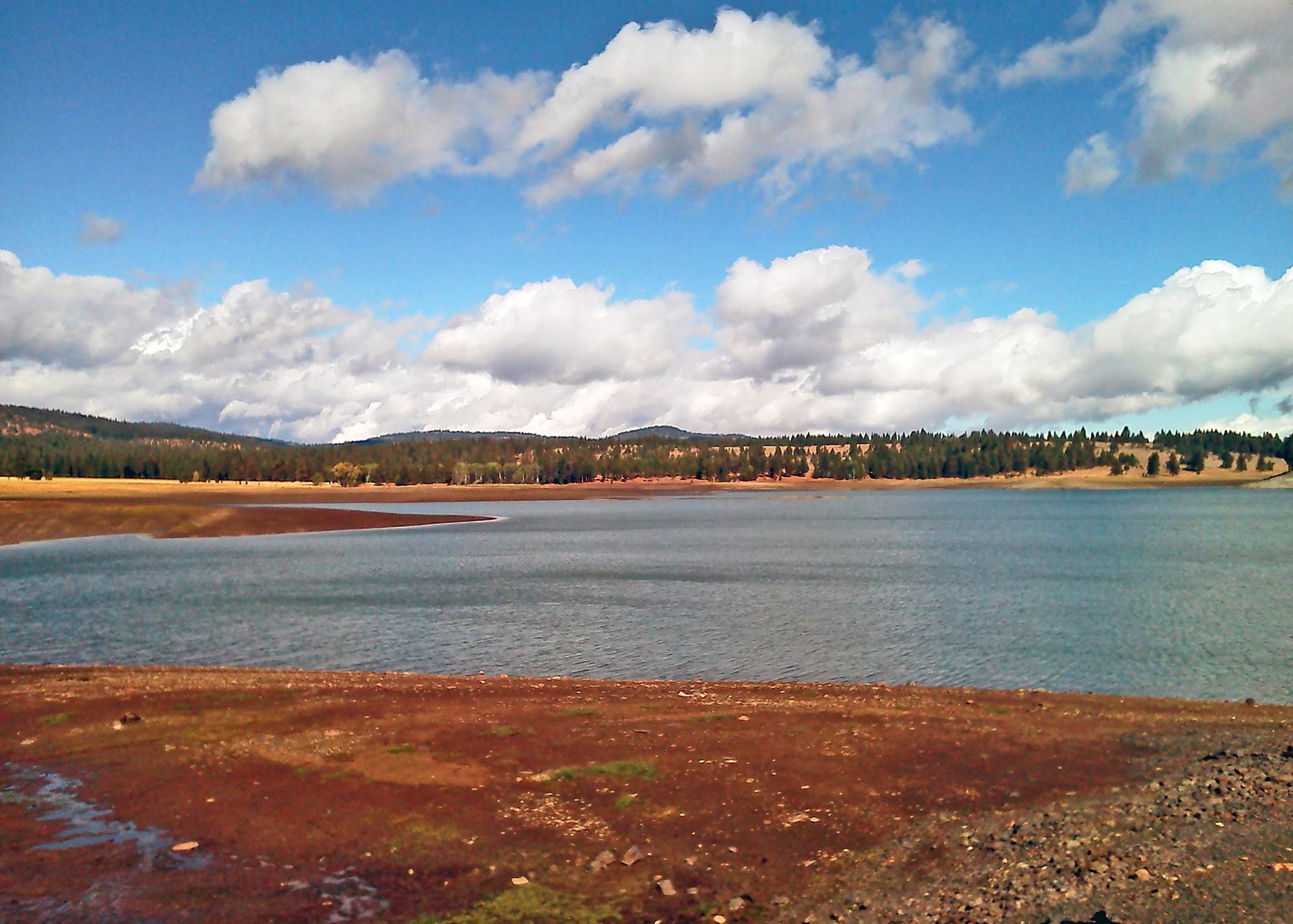 A wide lake with dry, reddish shores under a partly cloudy sky.