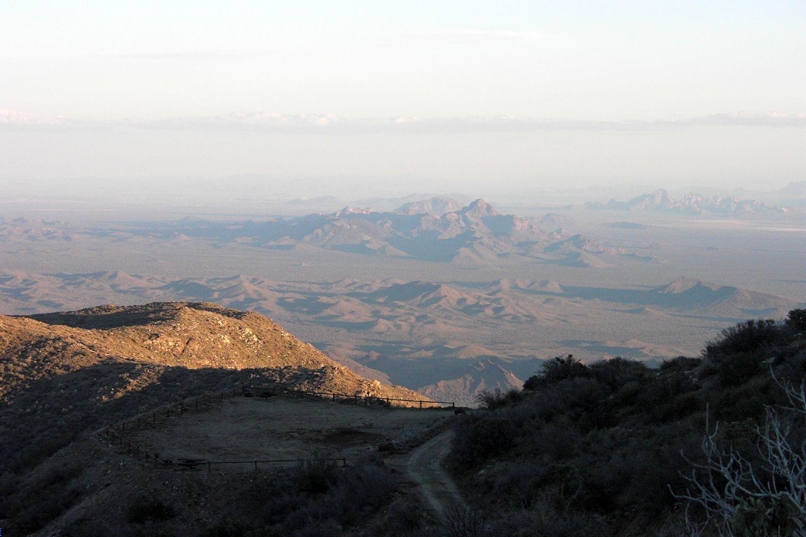 Hazy mountain landscape with golden light on foreground hills at sunrise.