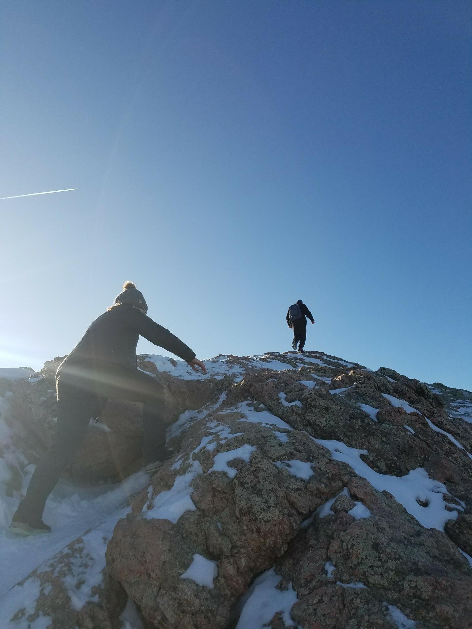 Two hikers ascending a snowy, rocky peak under bright sun.