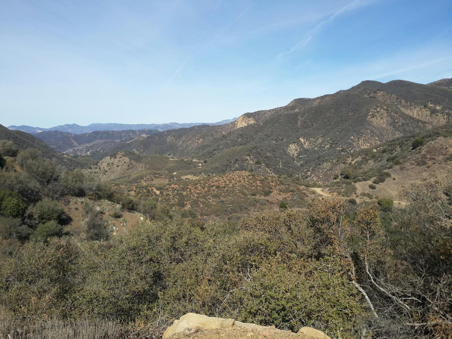 Expansive view of sunlit, rolling mountains and valleys with sparse vegetation.