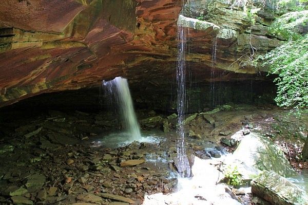 Two waterfalls cascade from a dark rock overhang into a rocky stream. - Glory Hole Falls Trail