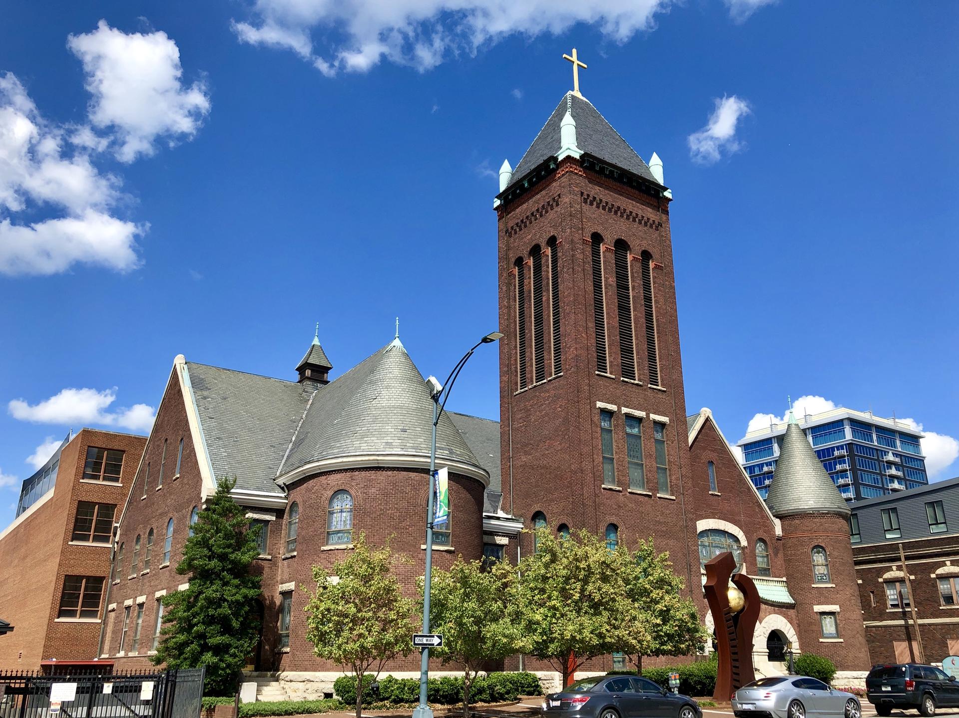 Large brick church with a tall steeple under a bright blue sky.