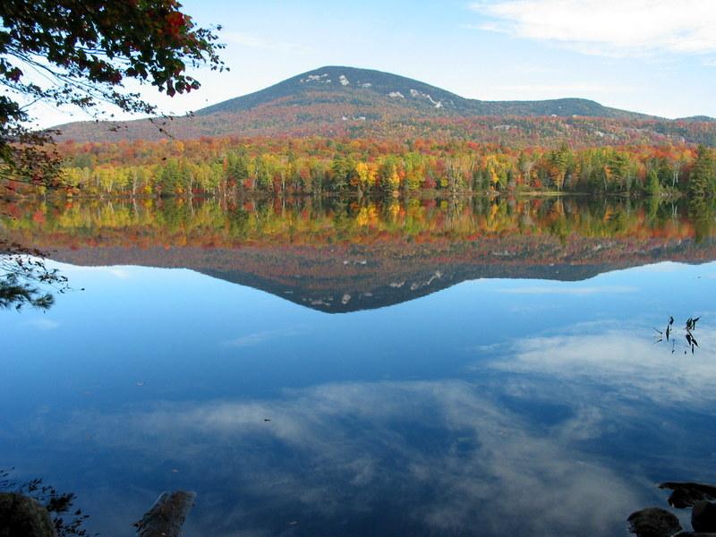 Vibrant autumn trees and a mountain reflect perfectly in a calm lake.