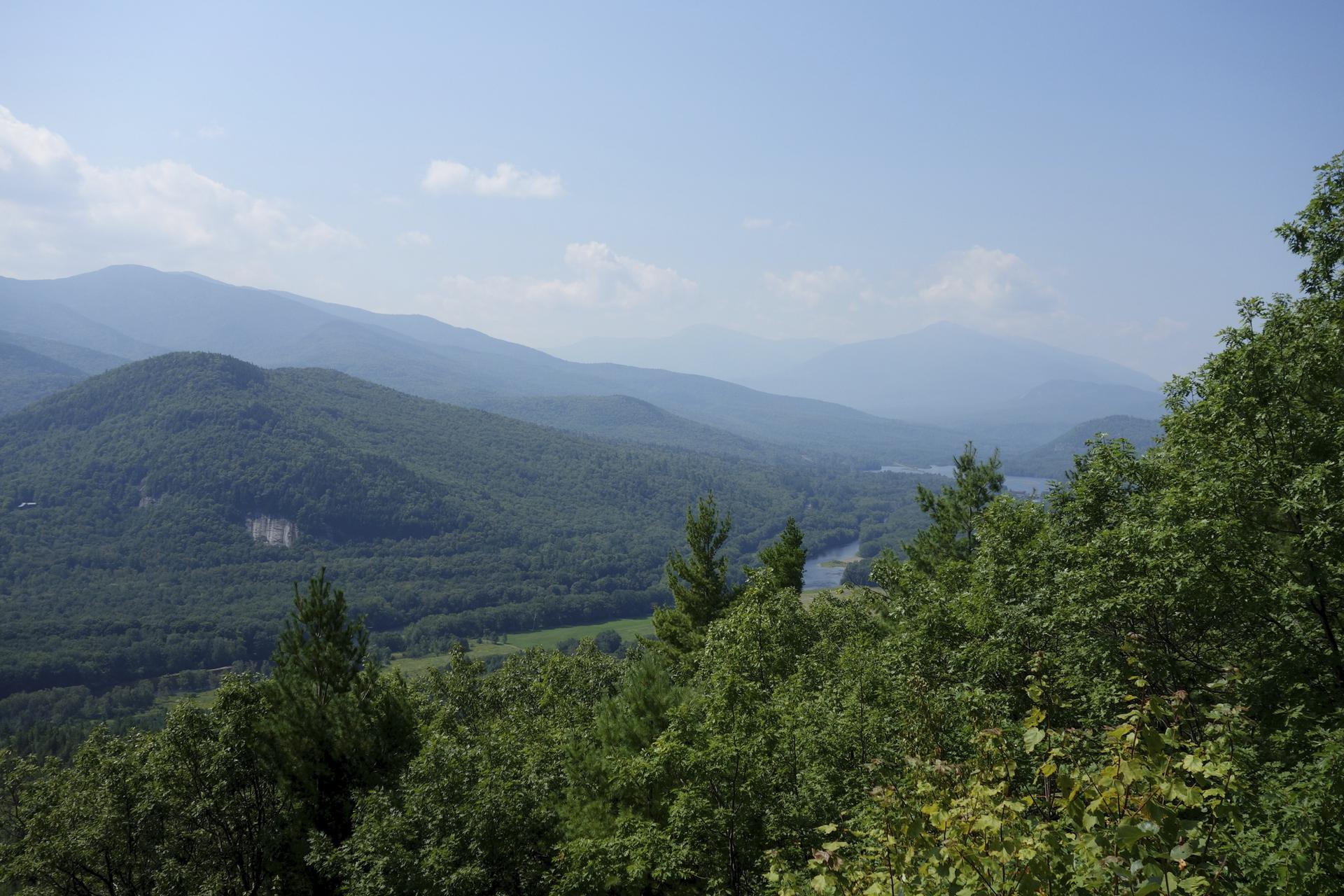 Panoramic view of vast forested mountains and valleys under a clear sky.