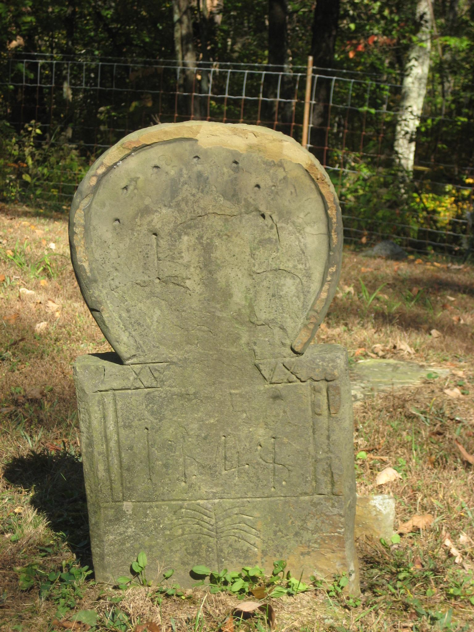 An old, weathered stone marker stands in a grassy, wooded area.