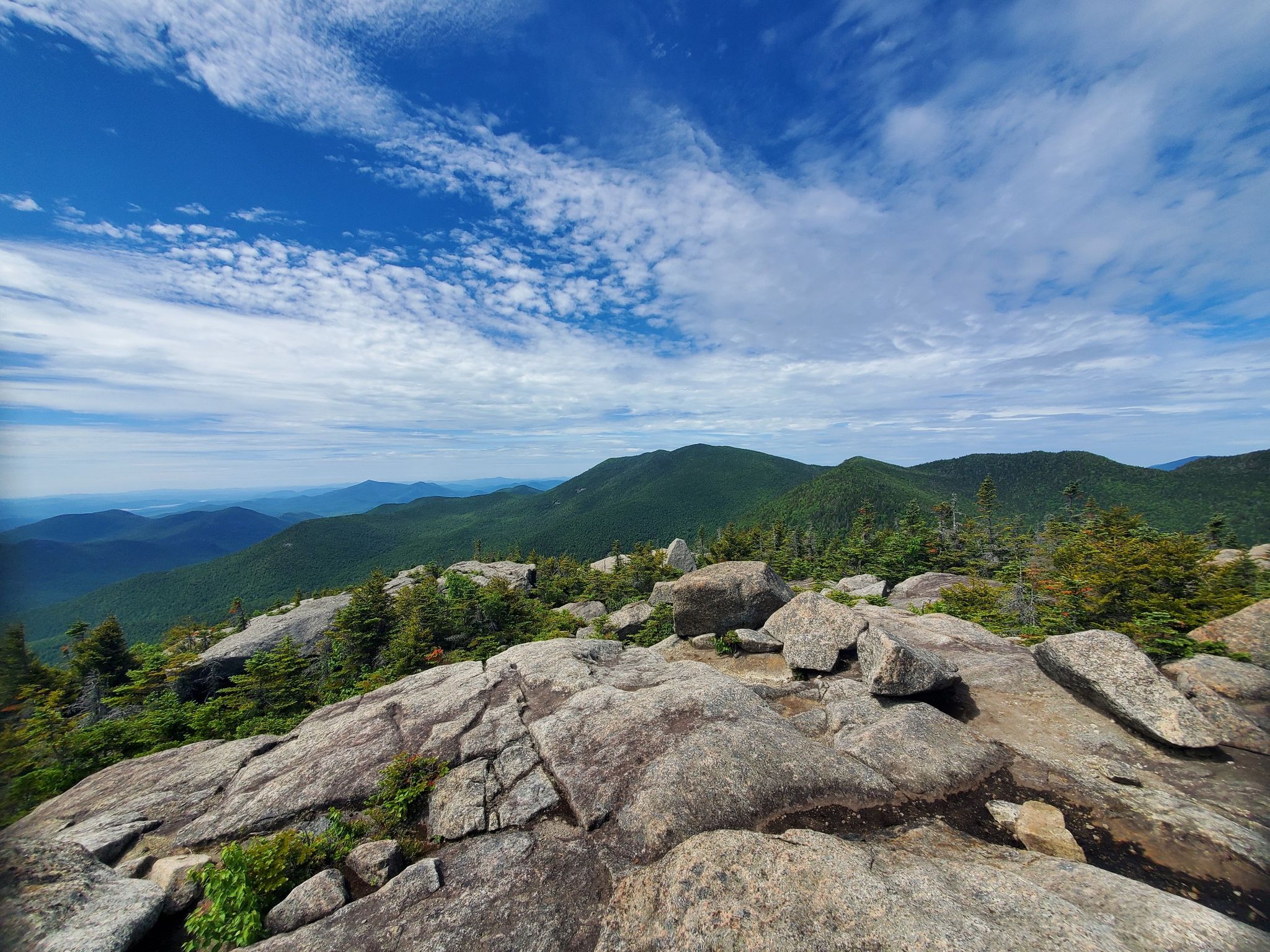 Sunny mountain view with rocky foreground, green peaks, and blue sky. - Dix Range Traverse
