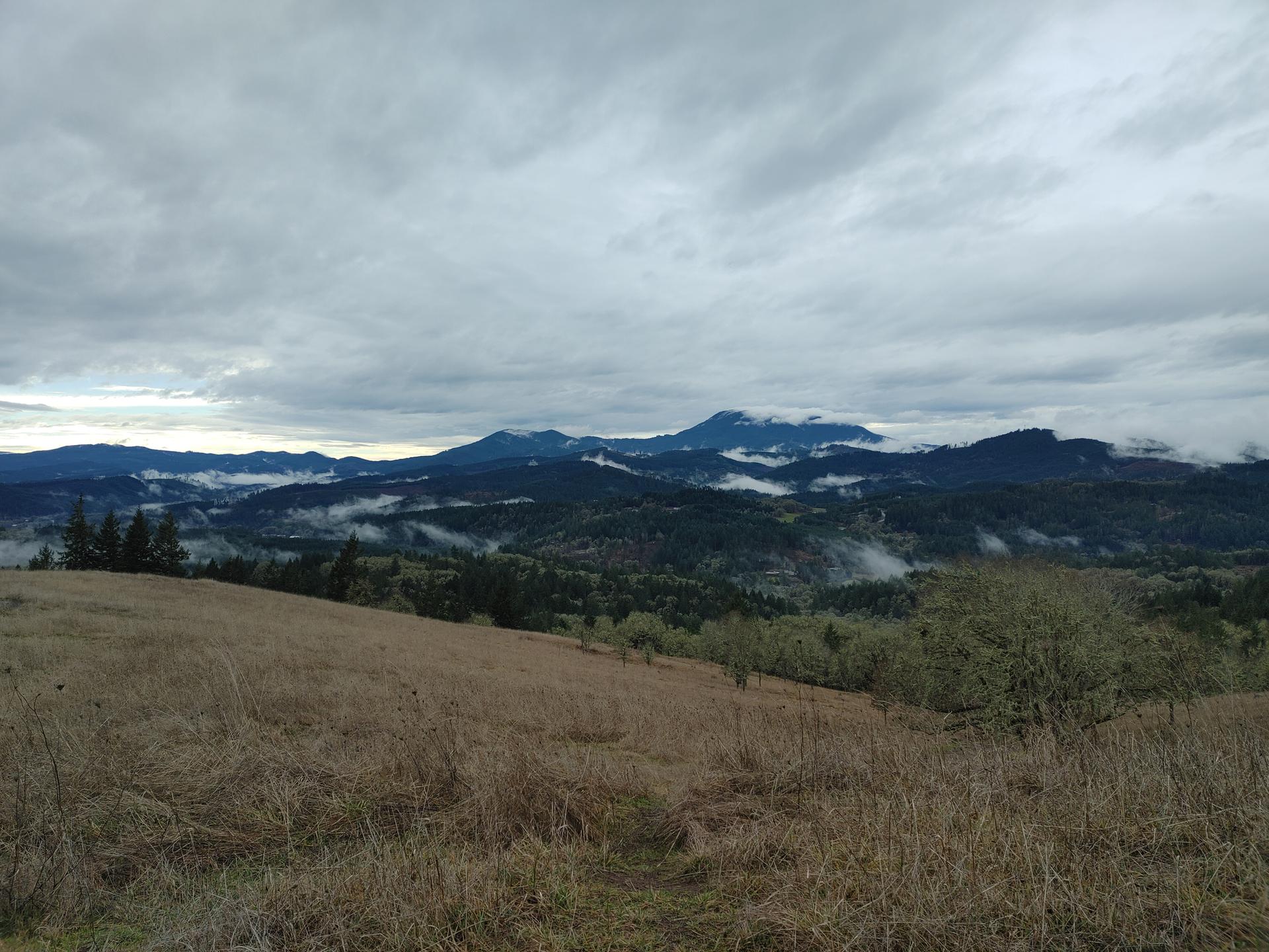 Panoramic view of cloudy mountains and misty valleys from a grassy hill.