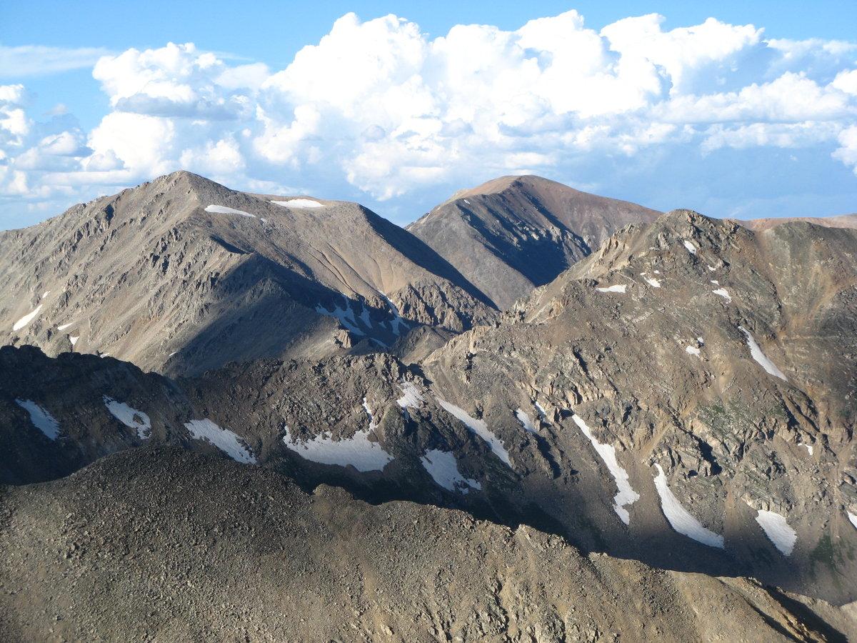 Rugged, rocky mountain peaks with snow patches under a bright blue sky.