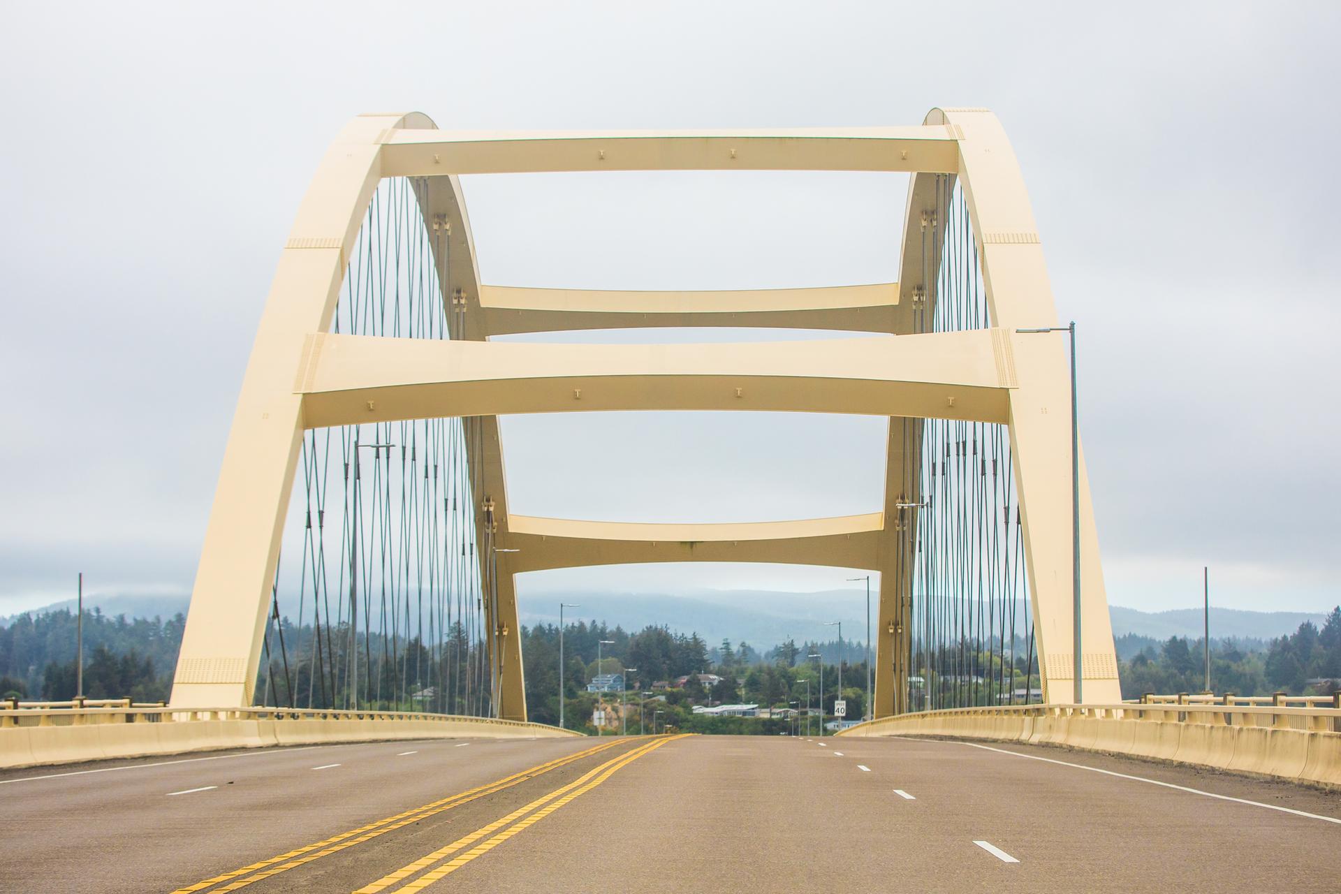 Driving across a large yellow concrete arch bridge on an overcast day.