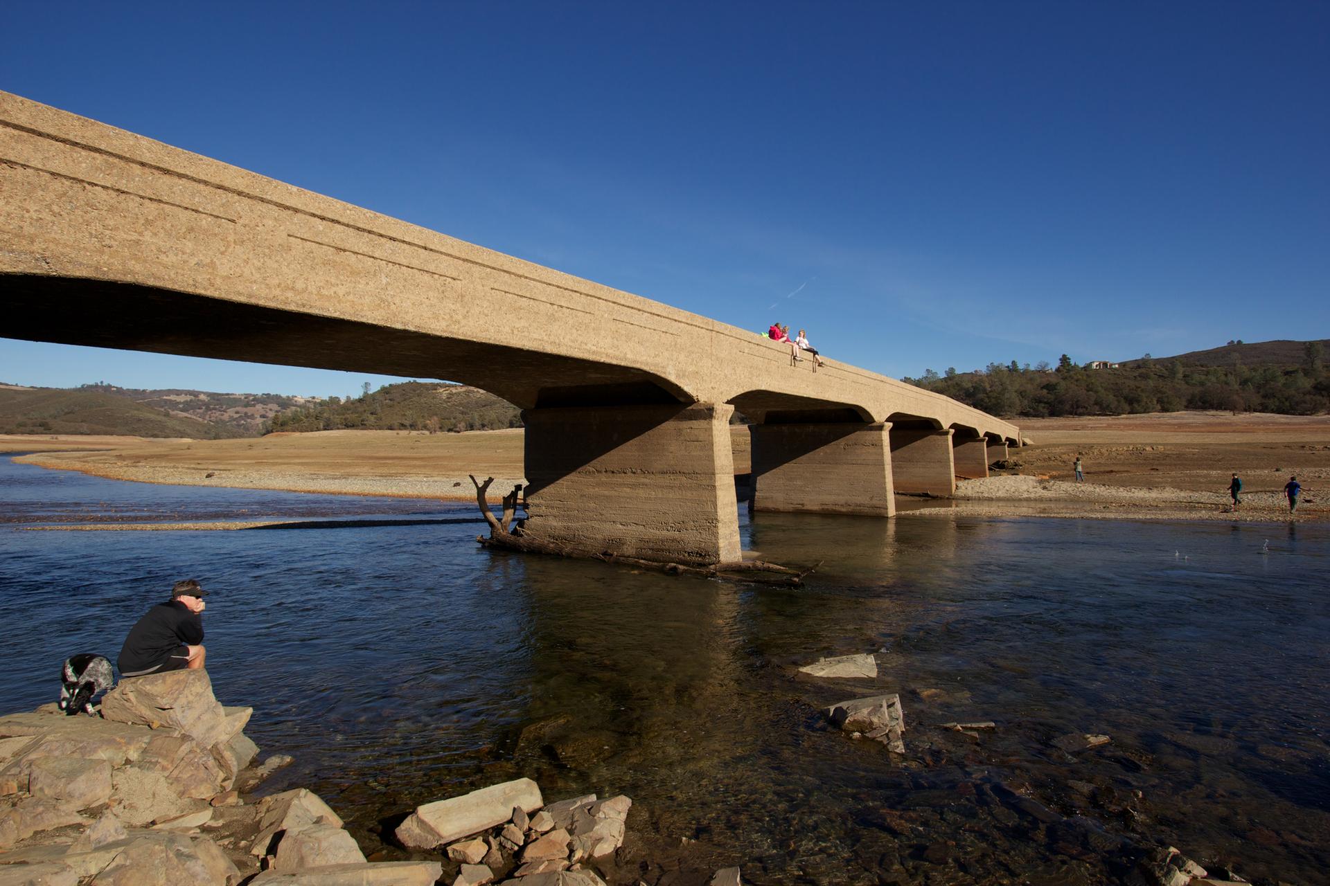 Large concrete bridge over water with people on the bank and bridge.