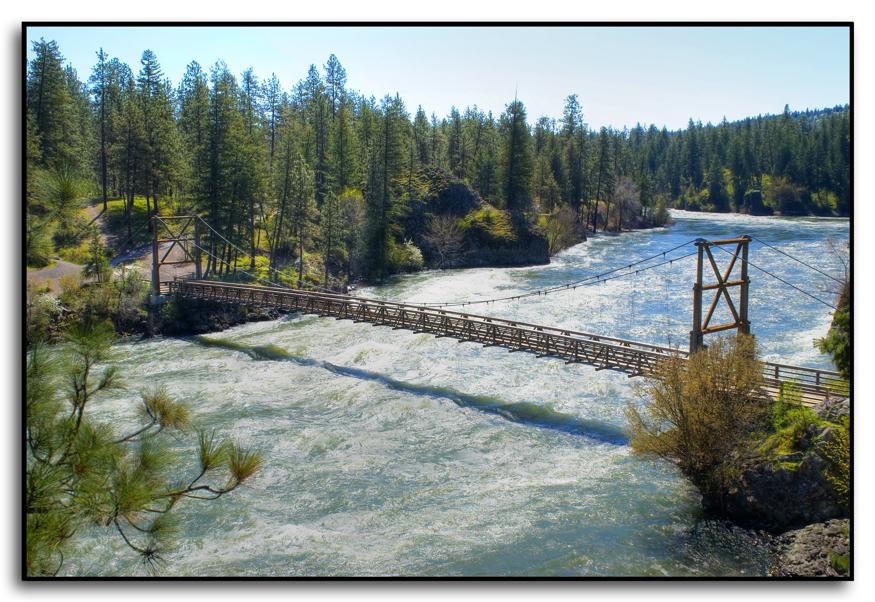 Long wooden suspension bridge over a wide, fast-flowing river.