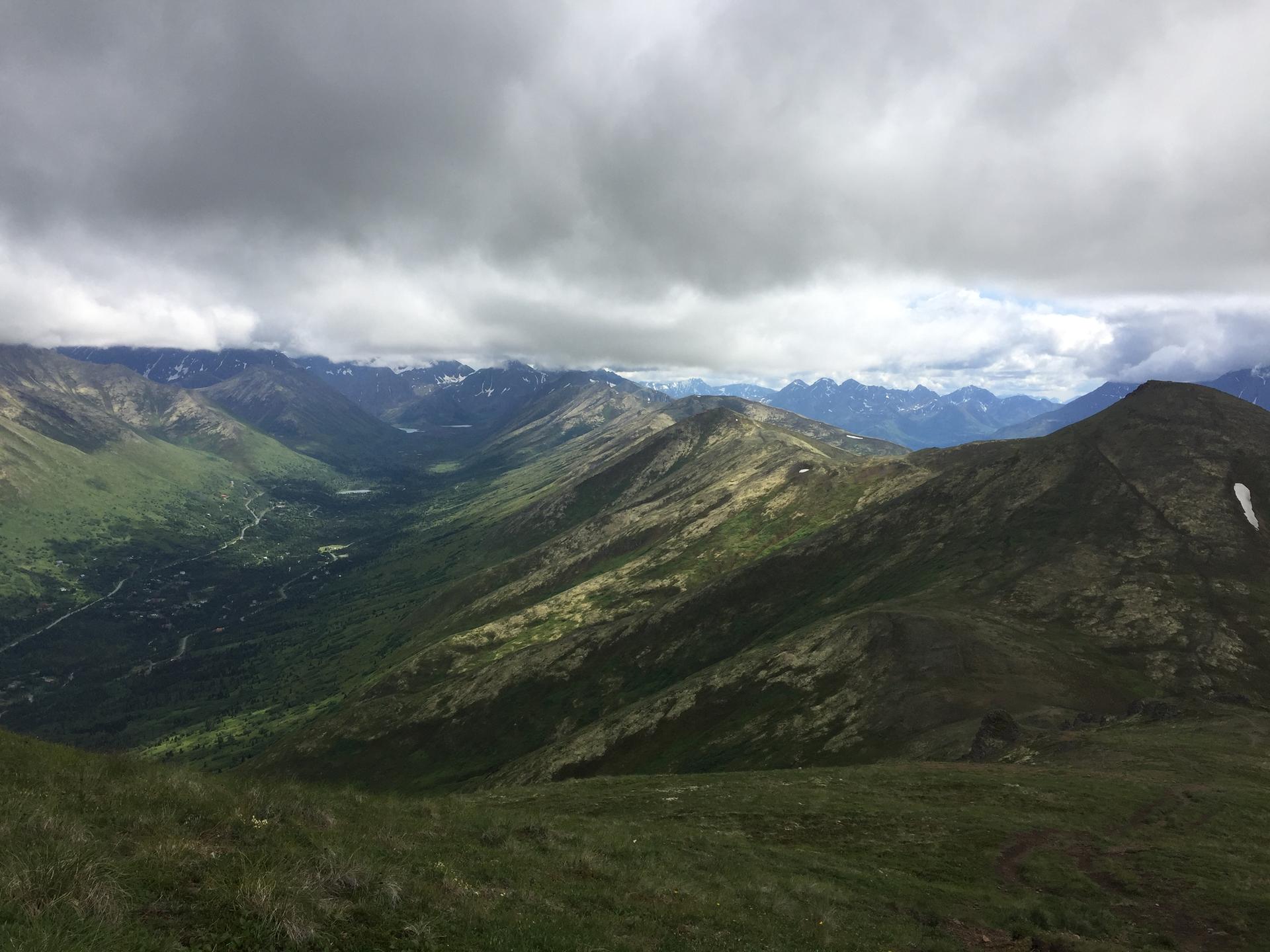 Expansive view of green mountain ranges and valleys under a cloudy sky.