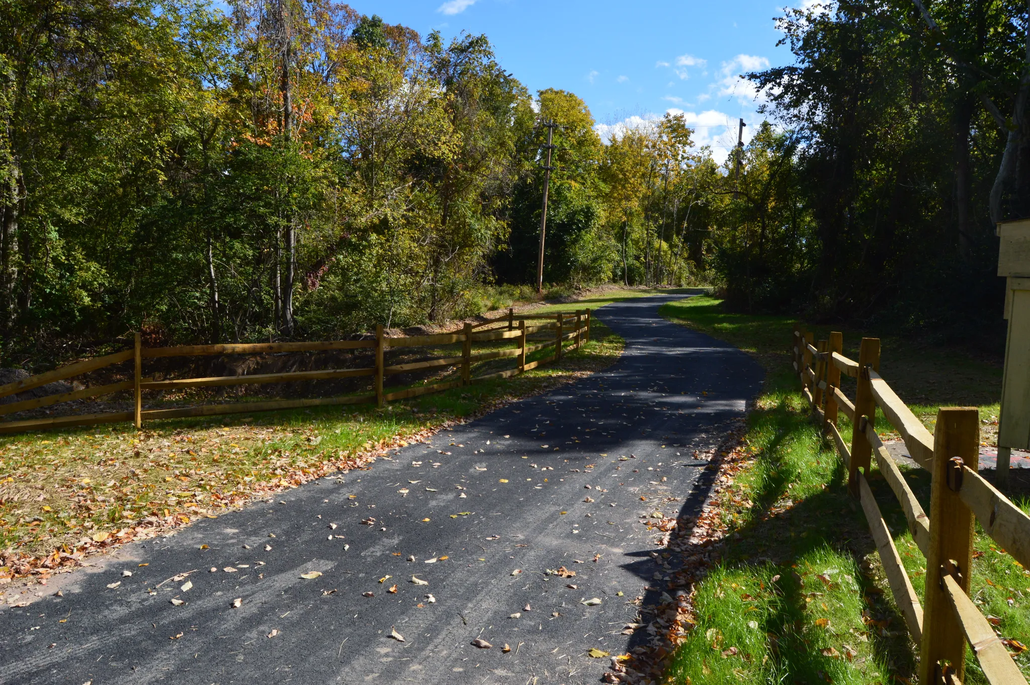 Paved path with wooden fences, autumn trees, and dappled sunlight. - Schuylkill River Trail