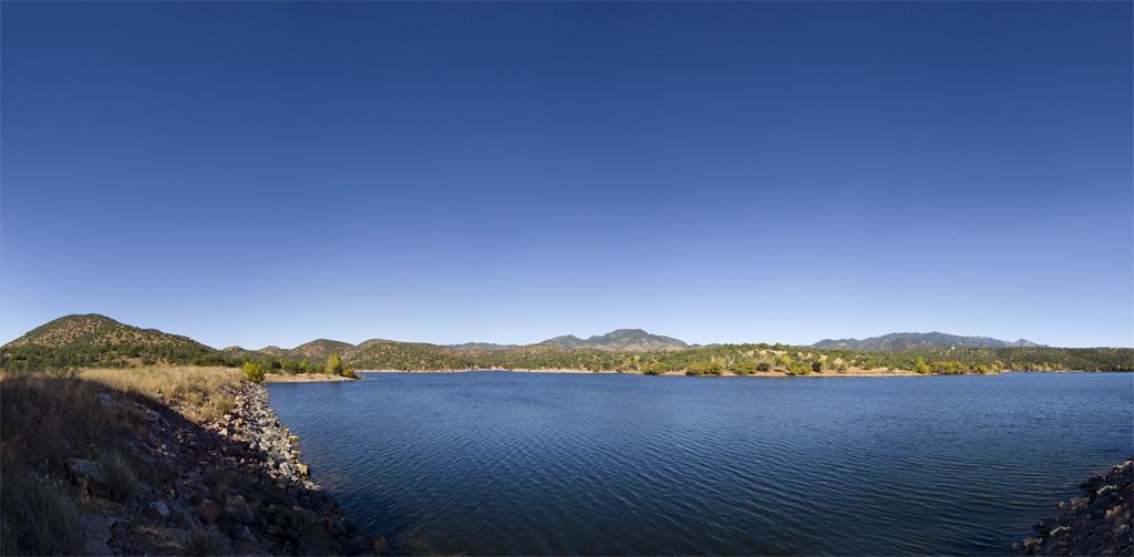 Wide panoramic view of a large lake surrounded by hills under a clear blue sky.