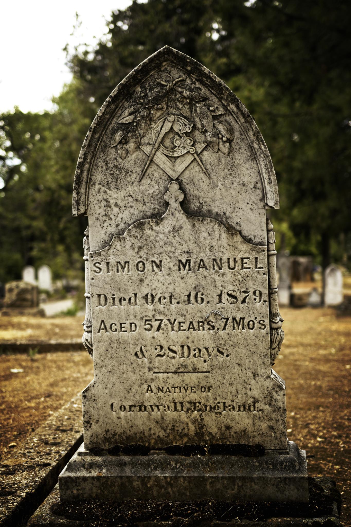 An old, weathered tombstone with Masonic symbols in a dim graveyard.