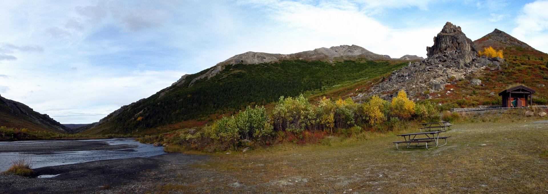 Panoramic view of a mountain valley with a river, autumn trees, and picnic tables.