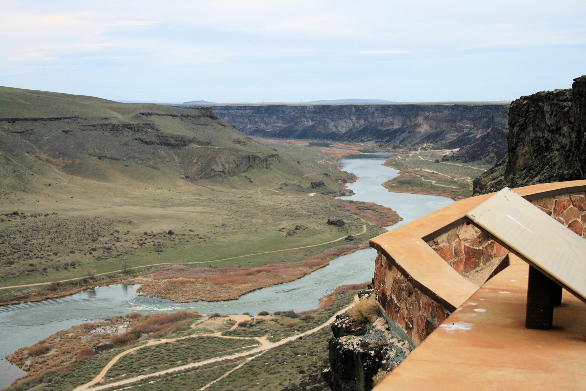 A winding river flows through a vast canyon under an overcast sky, seen from an overlook.