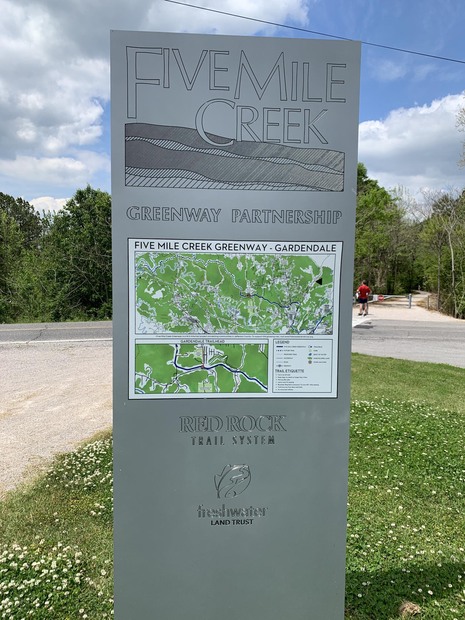 Tall informational sign with maps, person cycling in background.