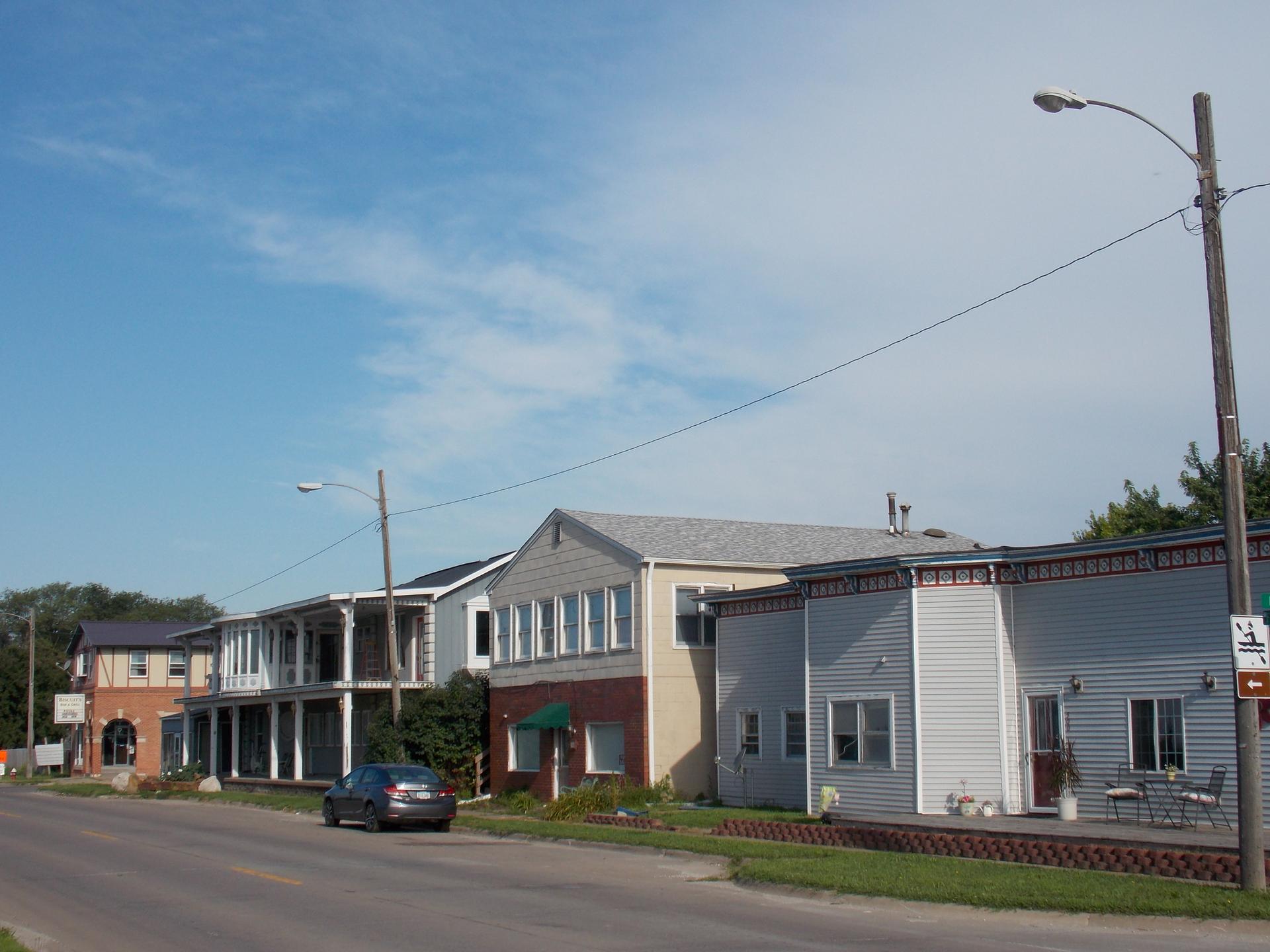 Row of buildings along a road under a bright blue sky with a parked car.