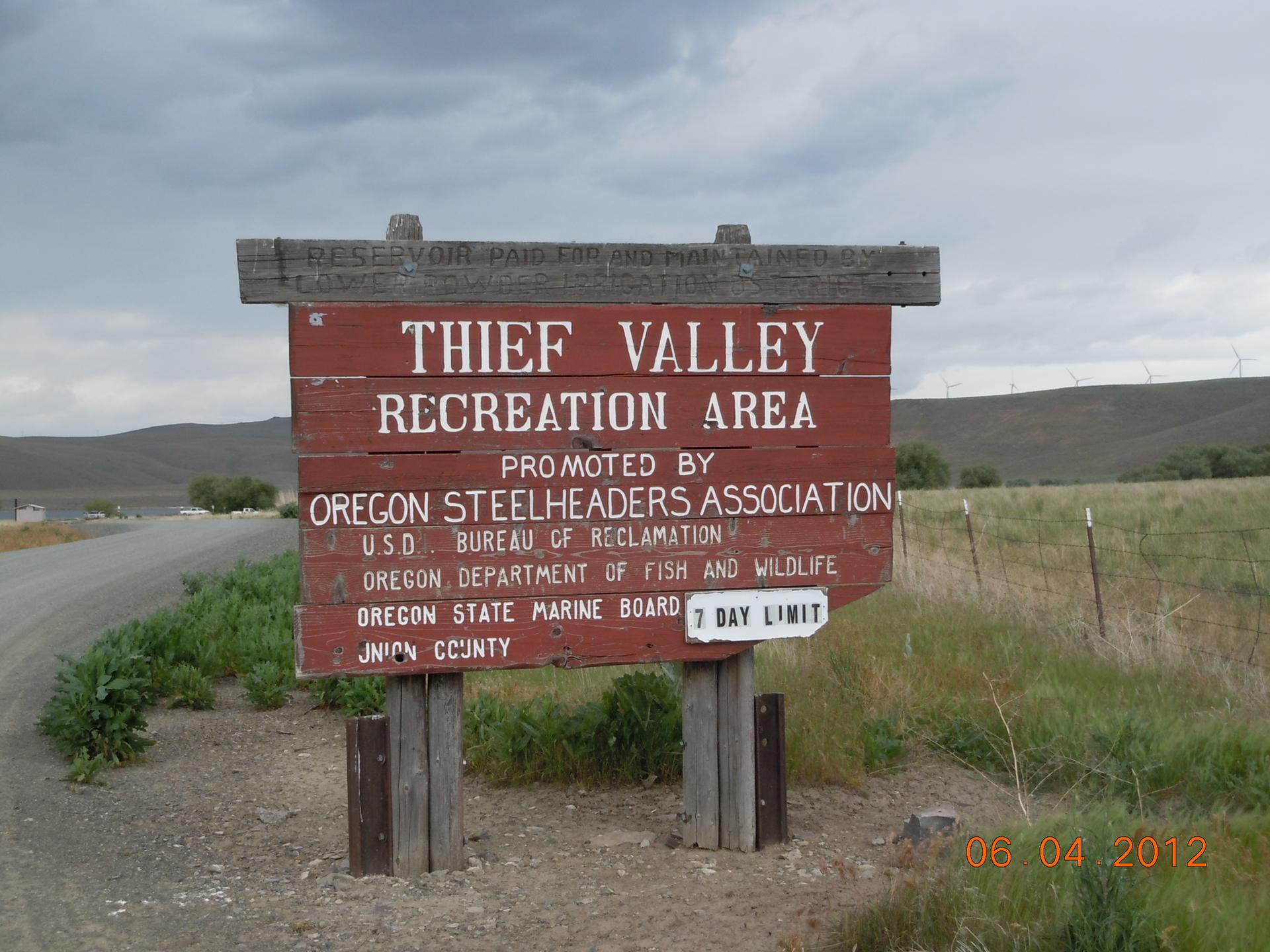 A rustic wooden sign stands beside a dirt road in a rural landscape.