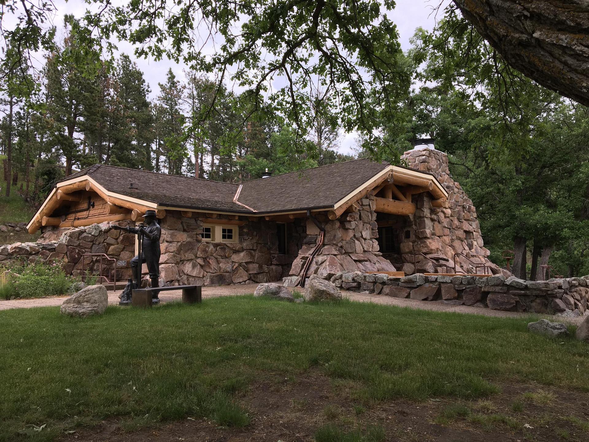 Rustic stone and log building with a statue by a water pump.