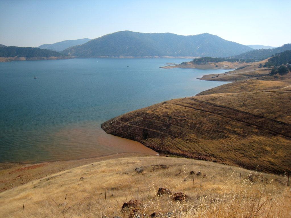 A large lake with boats, surrounded by dry, rolling hills under a clear sky.