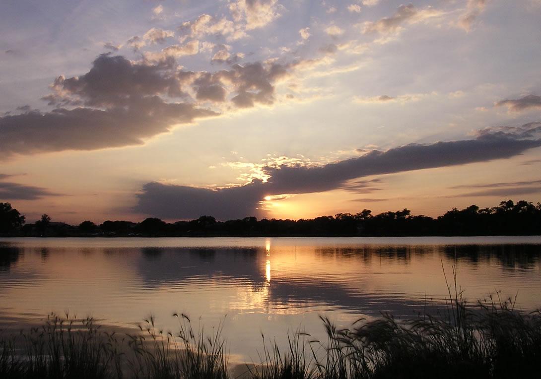 A serene lake reflects a colorful sunset with dark clouds and golden light.