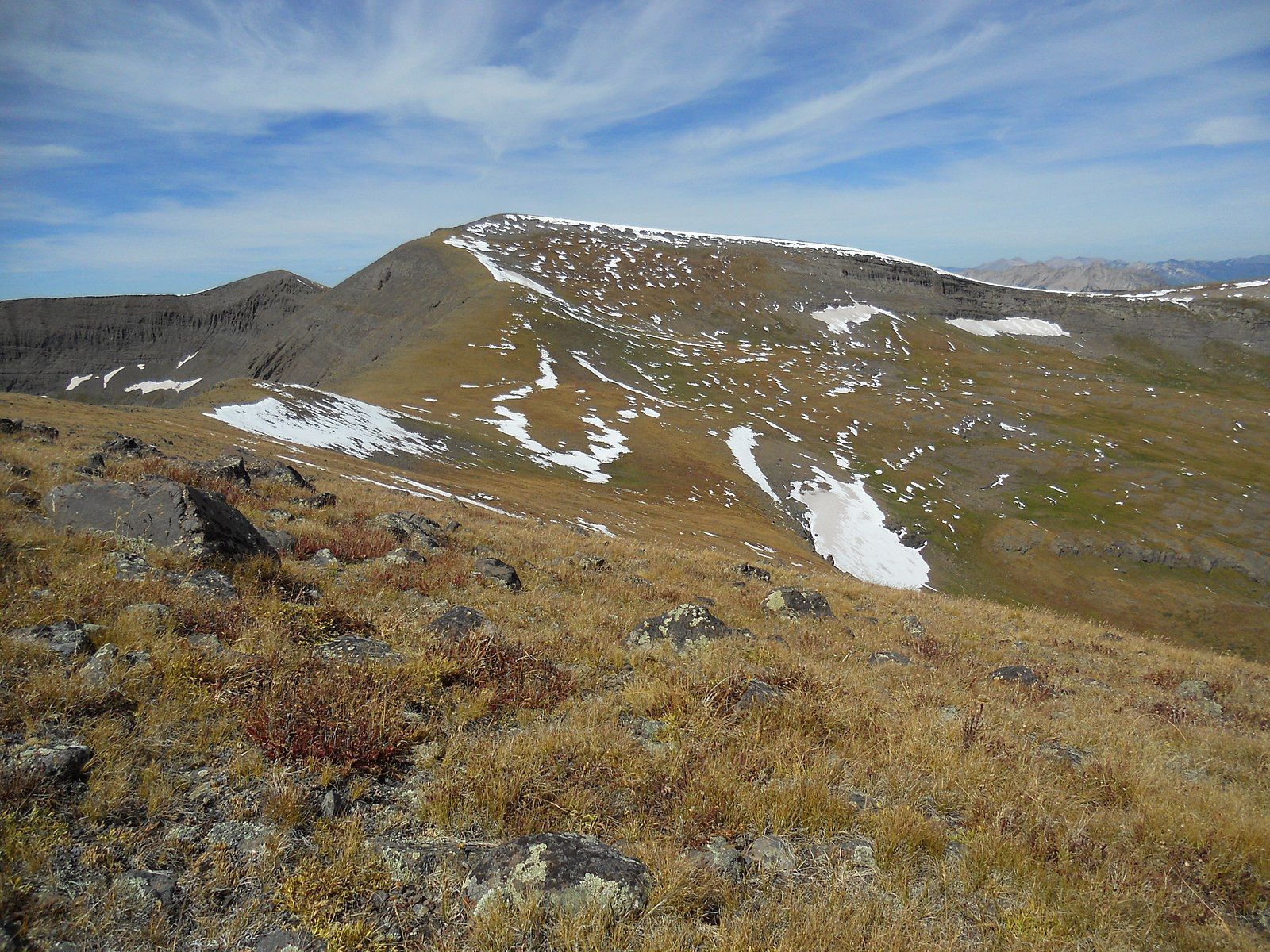 Expansive view of a rugged, treeless mountain landscape with snow patches under a blue sky. - Mill Castle Trail