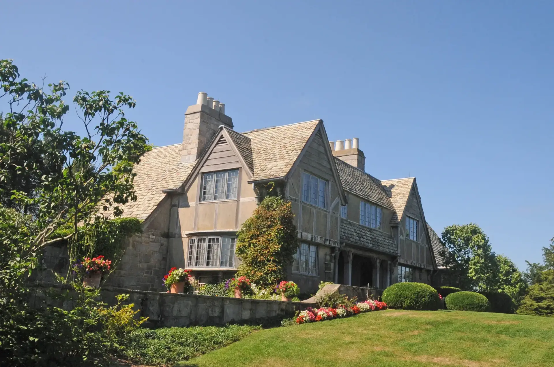 Large gabled house with stone walls and green landscaping under a clear blue sky.