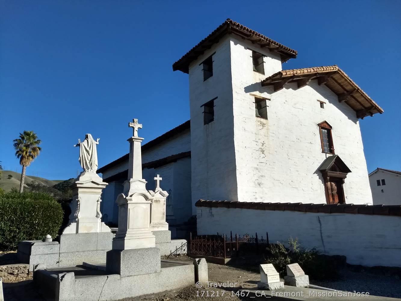 White stucco building with a tower, statues, and palm tree under blue sky.