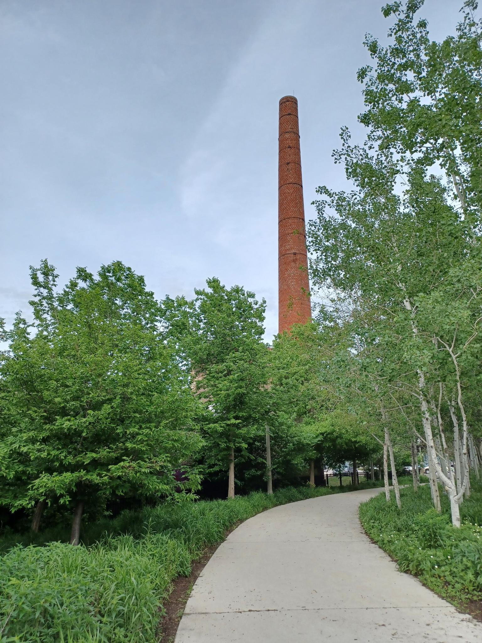 A tall brick chimney stands above a winding path and green trees.