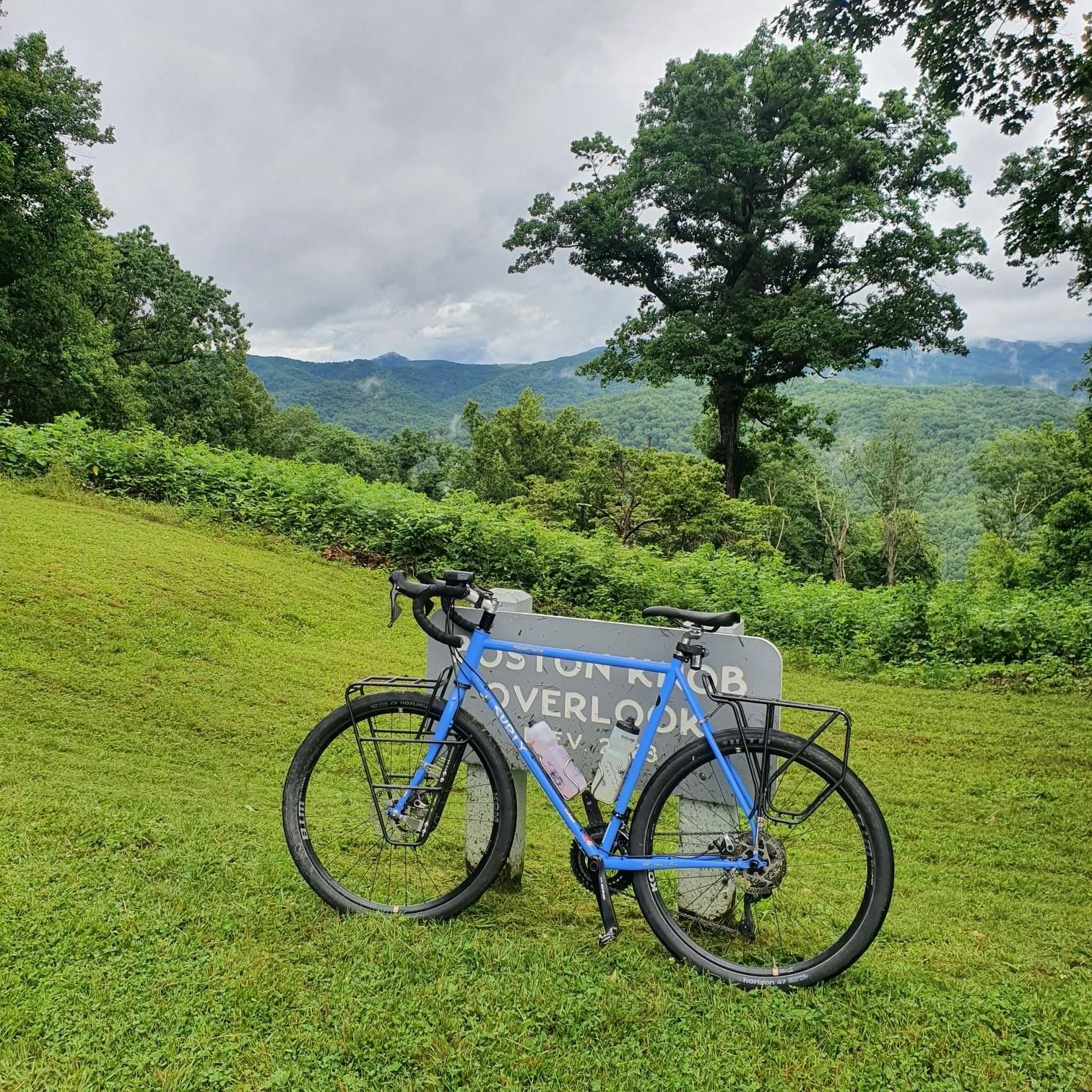 Blue bicycle on a grassy hill overlooking green mountains under an overcast sky. - Blue Ridge Parkway: Boston Knob